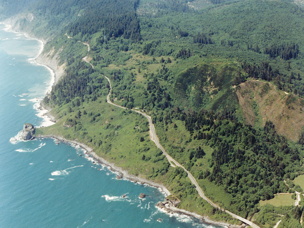 Aerial view of the road at Last Chance Grade winding through forest and along cliffs above the Pacific Ocean